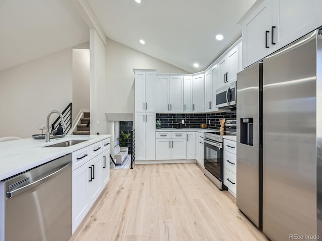 kitchen with light wood-style flooring, a sink, vaulted ceiling, appliances with stainless steel finishes, and tasteful backsplash