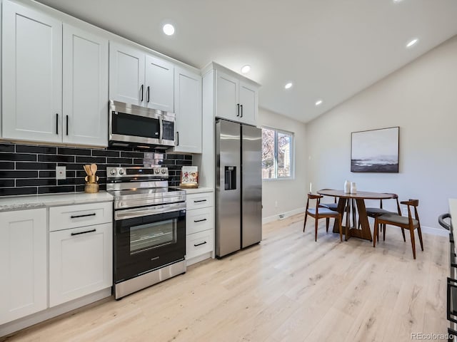 kitchen featuring lofted ceiling, light wood-type flooring, stainless steel appliances, and backsplash