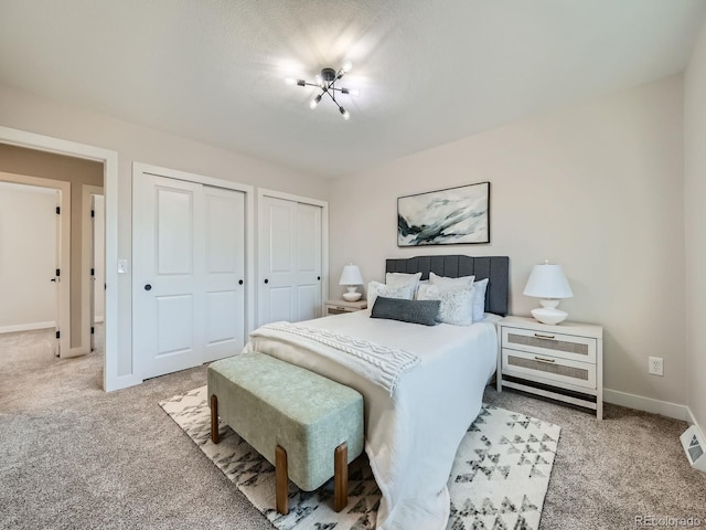 bedroom with light carpet, two closets, and baseboards