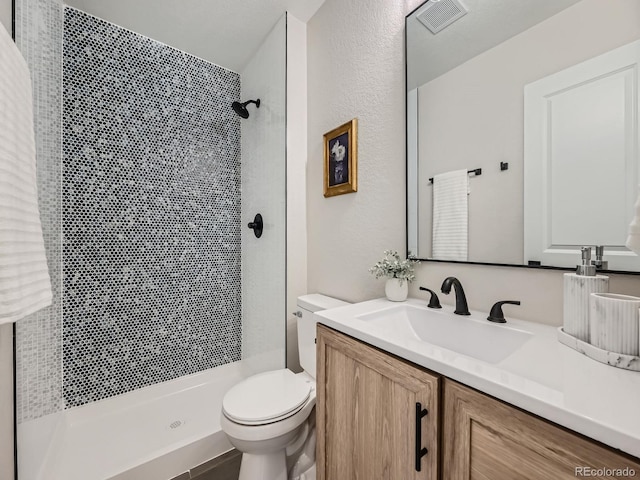 full bath featuring a stall shower, visible vents, a textured wall, toilet, and vanity