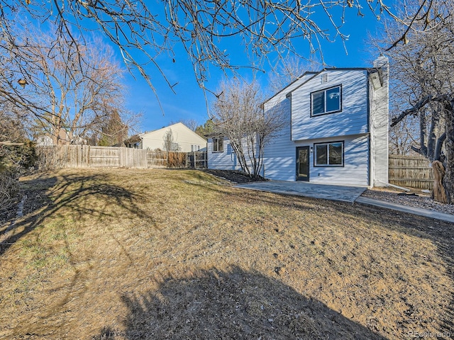 back of house featuring fence private yard, a patio area, a chimney, and a yard