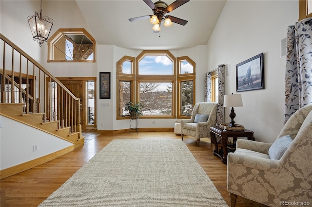 sitting room featuring a towering ceiling, light hardwood / wood-style flooring, and ceiling fan with notable chandelier