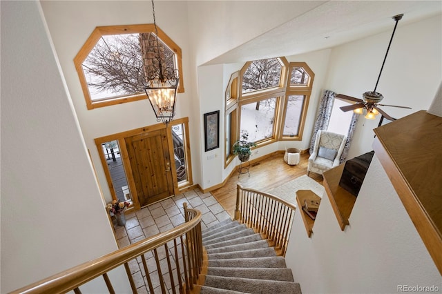 entrance foyer featuring a towering ceiling, a wealth of natural light, ceiling fan with notable chandelier, and light wood-type flooring