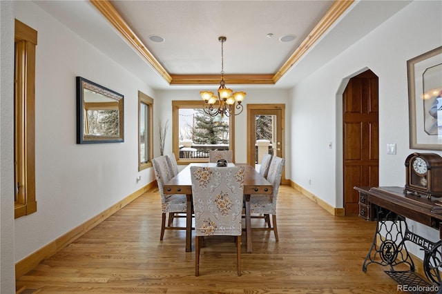 dining space featuring arched walkways, a chandelier, baseboards, light wood-type flooring, and a tray ceiling