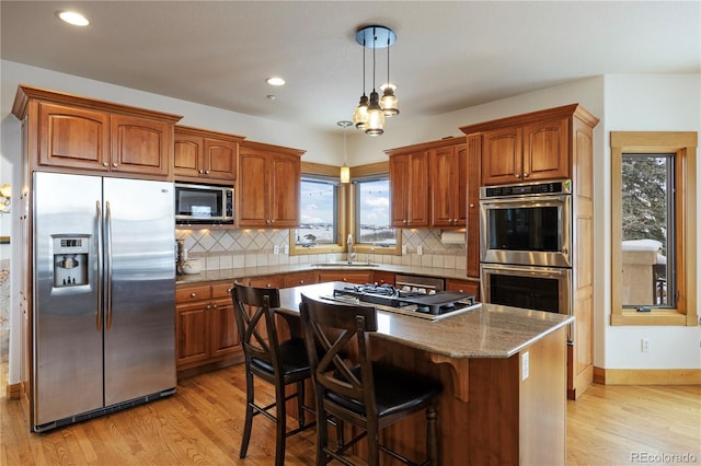 kitchen with sink, light hardwood / wood-style flooring, appliances with stainless steel finishes, a kitchen island, and backsplash