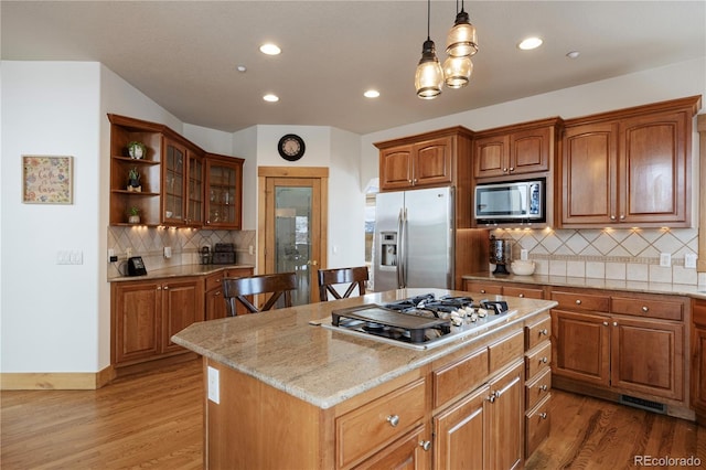 kitchen with light wood-type flooring, appliances with stainless steel finishes, glass insert cabinets, and decorative light fixtures