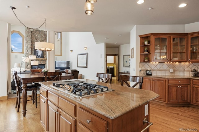 kitchen with light hardwood / wood-style flooring, a breakfast bar area, stainless steel gas cooktop, a kitchen island, and a stone fireplace