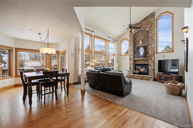 dining room with a stone fireplace, high vaulted ceiling, ceiling fan, and light wood-type flooring