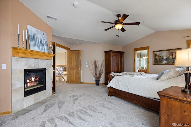 bedroom with a tile fireplace, ceiling fan, connected bathroom, light carpet, and vaulted ceiling