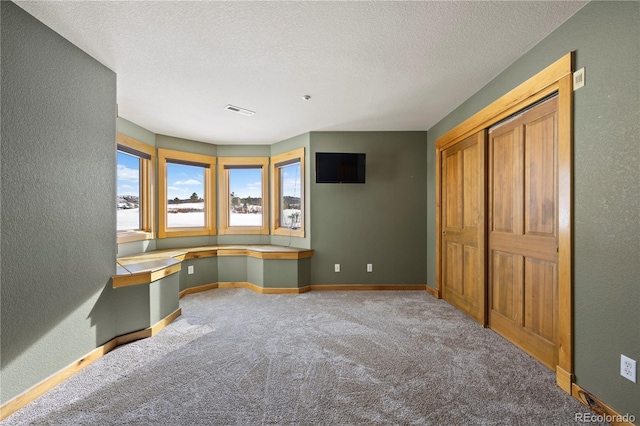 unfurnished office with baseboards, visible vents, a textured wall, carpet floors, and built in desk