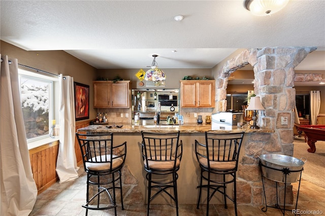 kitchen with a peninsula, a textured ceiling, ornate columns, a kitchen bar, and backsplash