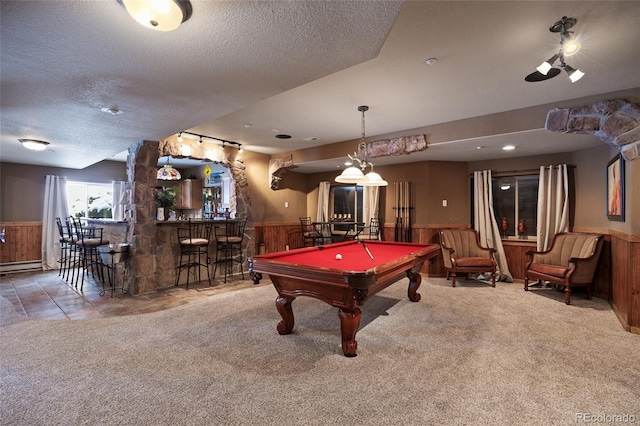 playroom with a textured ceiling, carpet floors, wood walls, wainscoting, and a bar