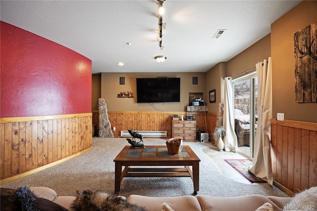 carpeted living room with a baseboard radiator, rail lighting, a textured ceiling, and wood walls