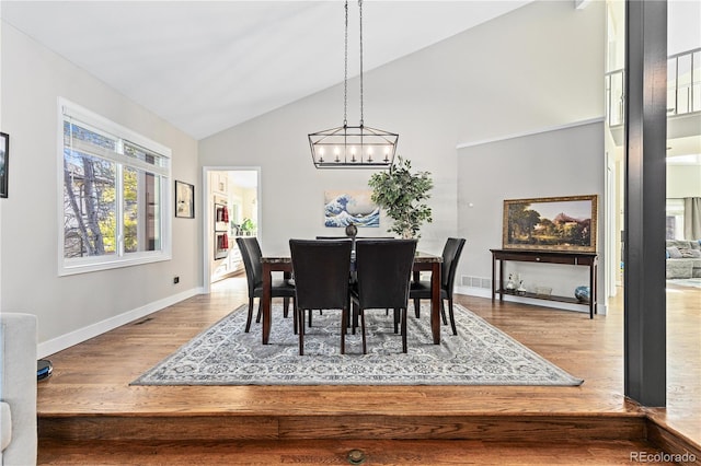 dining space featuring wood-type flooring, high vaulted ceiling, and a notable chandelier