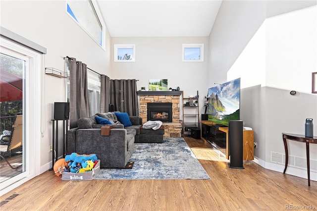 living area with a stone fireplace, light hardwood / wood-style floors, a healthy amount of sunlight, and a towering ceiling