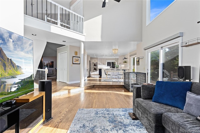 living room with a high ceiling, ceiling fan, and light hardwood / wood-style flooring