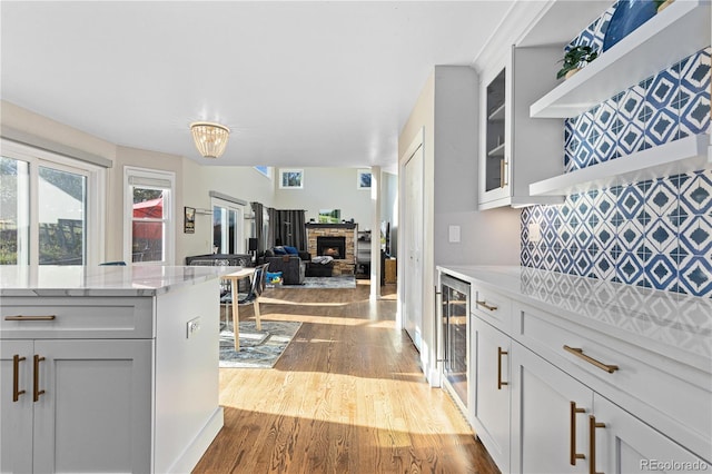 kitchen featuring light stone counters, wine cooler, wood-type flooring, decorative backsplash, and a stone fireplace