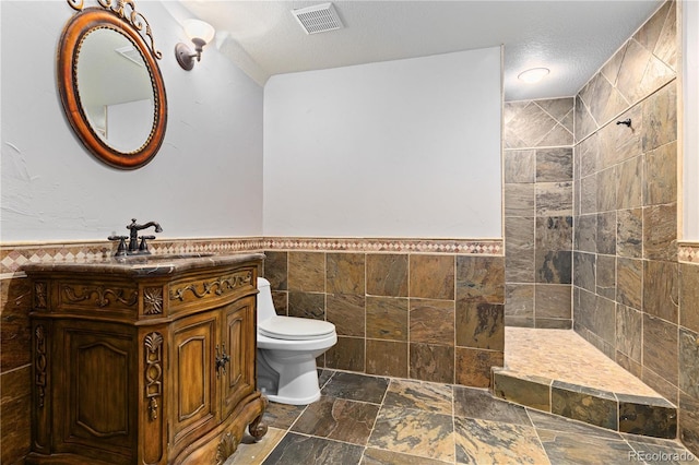 bathroom featuring a tile shower, tile walls, vanity, toilet, and a textured ceiling