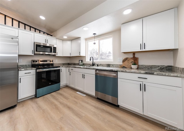 kitchen with pendant lighting, appliances with stainless steel finishes, sink, white cabinetry, and lofted ceiling