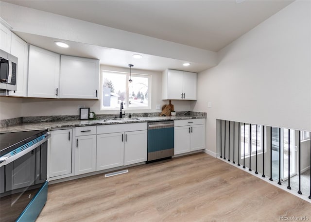 kitchen featuring appliances with stainless steel finishes, white cabinetry, dark stone countertops, light hardwood / wood-style floors, and sink