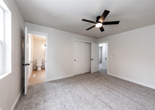 unfurnished bedroom with a textured ceiling, connected bathroom, a closet, carpet flooring, and ceiling fan