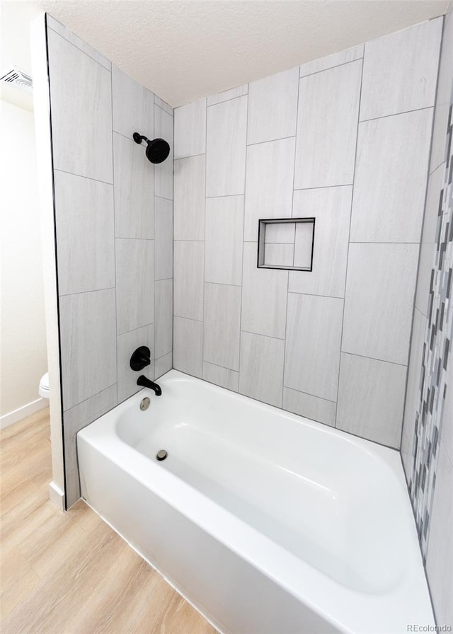 bathroom featuring wood-type flooring, toilet, a textured ceiling, and tiled shower / bath combo