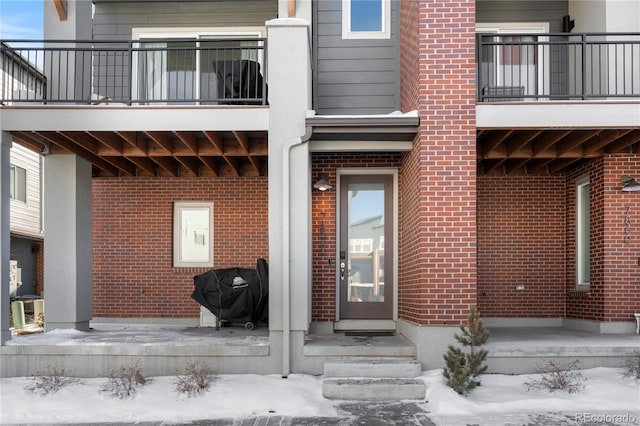 snow covered property entrance with brick siding and a balcony