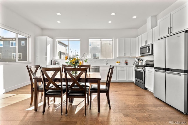 kitchen with light wood finished floors, appliances with stainless steel finishes, backsplash, white cabinetry, and a sink