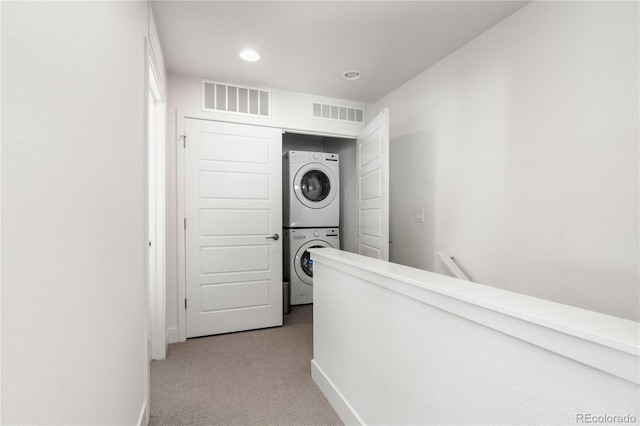 hallway featuring baseboards, visible vents, stacked washer / dryer, and light colored carpet