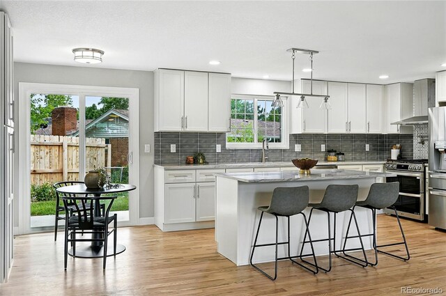 10320 W 35th Ave, Wheat Ridge, CO 80033 - kitchen with appliances with stainless steel finishes, wall chimney range hood, healthy amount of natural light, a breakfast bar area, and recessed lighting