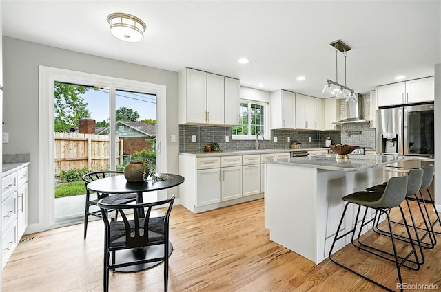 10320 W 35th Ave, Wheat Ridge, CO 80033 - kitchen with wall chimney exhaust hood, a kitchen bar, light wood-style floors, decorative backsplash, and a center island