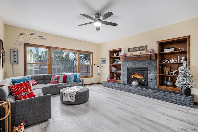 living room with built in shelves, ceiling fan, a fireplace, and light hardwood / wood-style floors