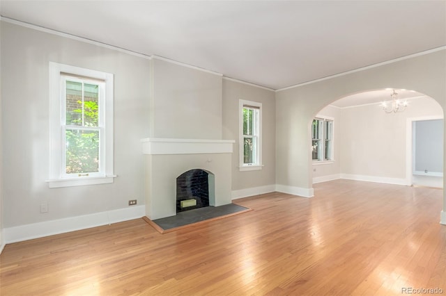 unfurnished living room featuring crown molding, a wealth of natural light, a notable chandelier, and light hardwood / wood-style floors