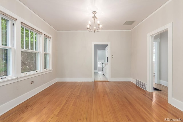 spare room featuring light wood-type flooring, an inviting chandelier, crown molding, and a healthy amount of sunlight