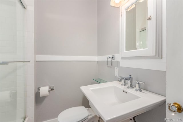 bathroom featuring a shower with door, toilet, and sink