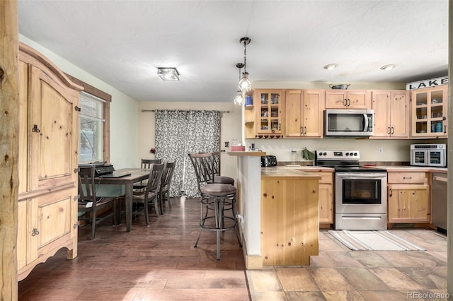 kitchen with appliances with stainless steel finishes, light brown cabinetry, a kitchen breakfast bar, hanging light fixtures, and dark hardwood / wood-style floors