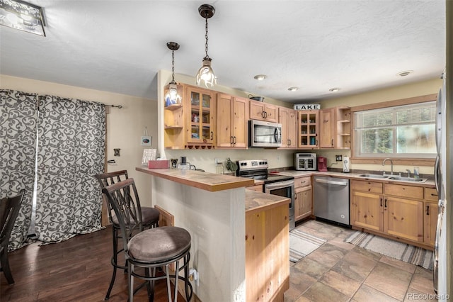 kitchen featuring kitchen peninsula, appliances with stainless steel finishes, hanging light fixtures, a breakfast bar, and sink