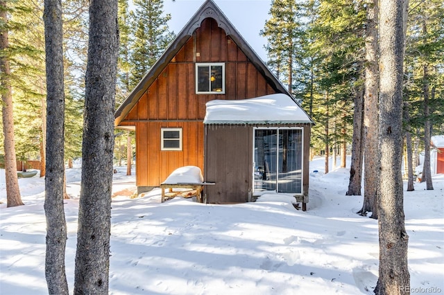 snow covered rear of property featuring an outbuilding