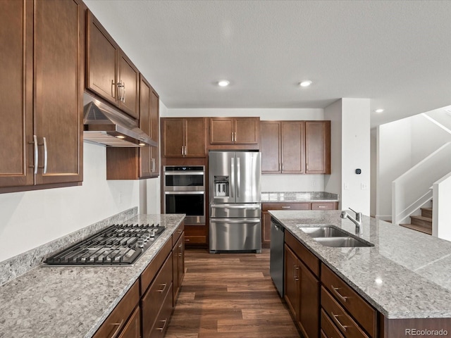 17843 W 93rd Pl, Arvada, CO 80007 - kitchen with stainless steel appliances, under cabinet range hood, dark wood-style flooring, light stone counters, and a kitchen island with sink