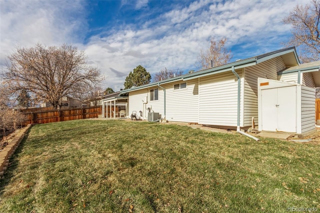 rear view of property featuring a lawn, central air condition unit, and a storage unit