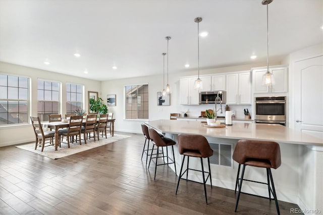 kitchen with a breakfast bar area, white cabinets, hanging light fixtures, and appliances with stainless steel finishes