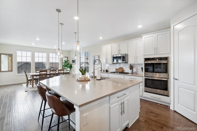 kitchen featuring pendant lighting, a kitchen island with sink, sink, appliances with stainless steel finishes, and white cabinetry