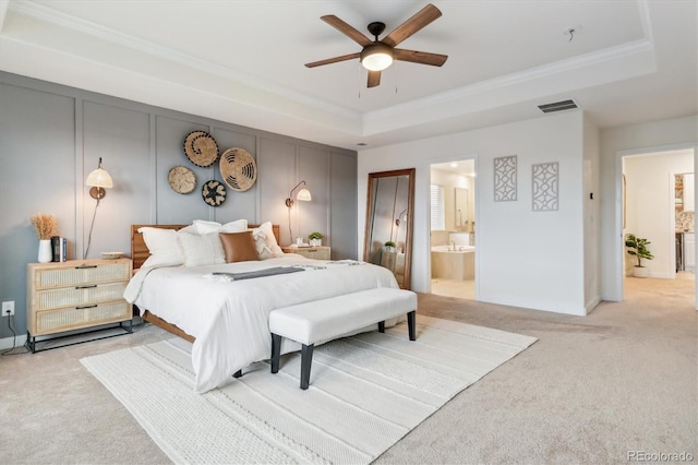 bedroom featuring ensuite bathroom, a tray ceiling, light colored carpet, ceiling fan, and crown molding