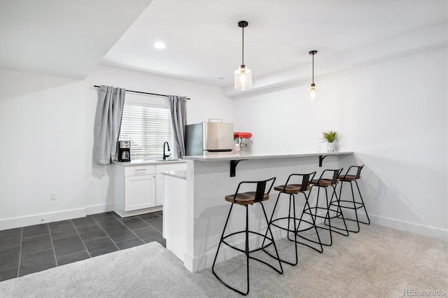 kitchen featuring kitchen peninsula, stainless steel fridge, a breakfast bar, decorative light fixtures, and white cabinetry