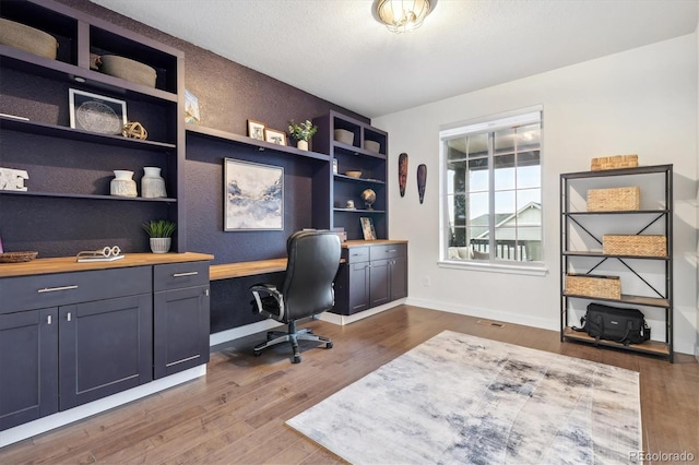 office featuring hardwood / wood-style floors, built in desk, and a textured ceiling