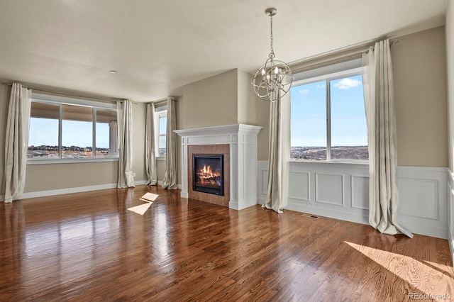 unfurnished living room with a notable chandelier, wood-type flooring, and a tiled fireplace