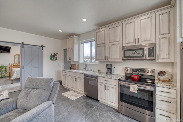 kitchen featuring light stone counters, a barn door, sink, stainless steel appliances, and dark colored carpet