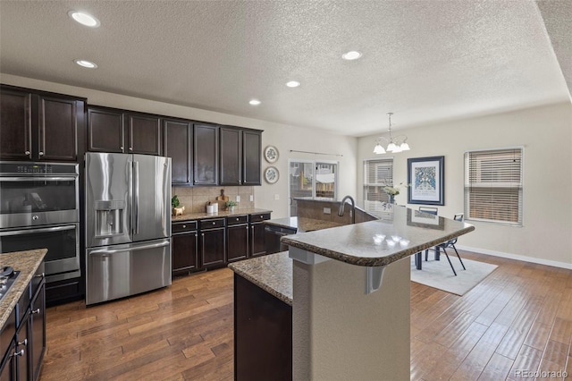 10414 Declaration Dr, Colorado Springs, CO 80925 - kitchen with stainless steel appliances, a textured ceiling, a chandelier, dark wood finished floors, and backsplash