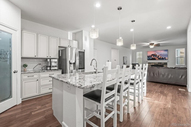 kitchen with stainless steel fridge with ice dispenser, dark wood-type flooring, ceiling fan, open floor plan, and light stone countertops
