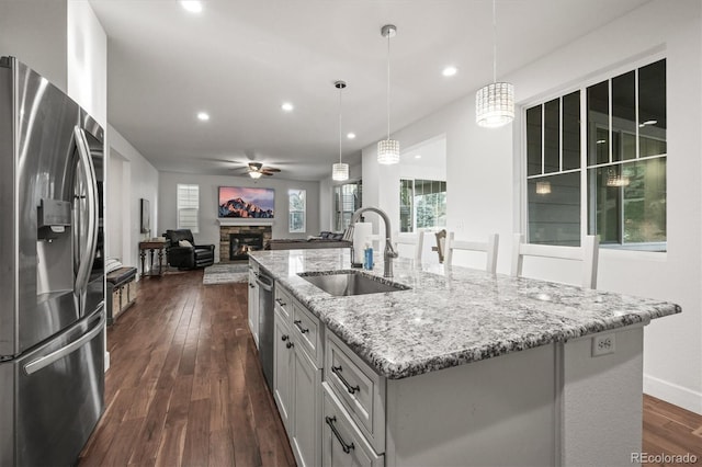 kitchen with appliances with stainless steel finishes, a sink, open floor plan, a stone fireplace, and ceiling fan